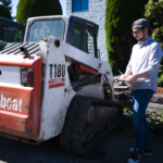 A supervisor in a hard hat and reflective vest carefully diagnoses a skid steer bobcat's issue, exemplifying hands-on expertise and problem-solving in action.