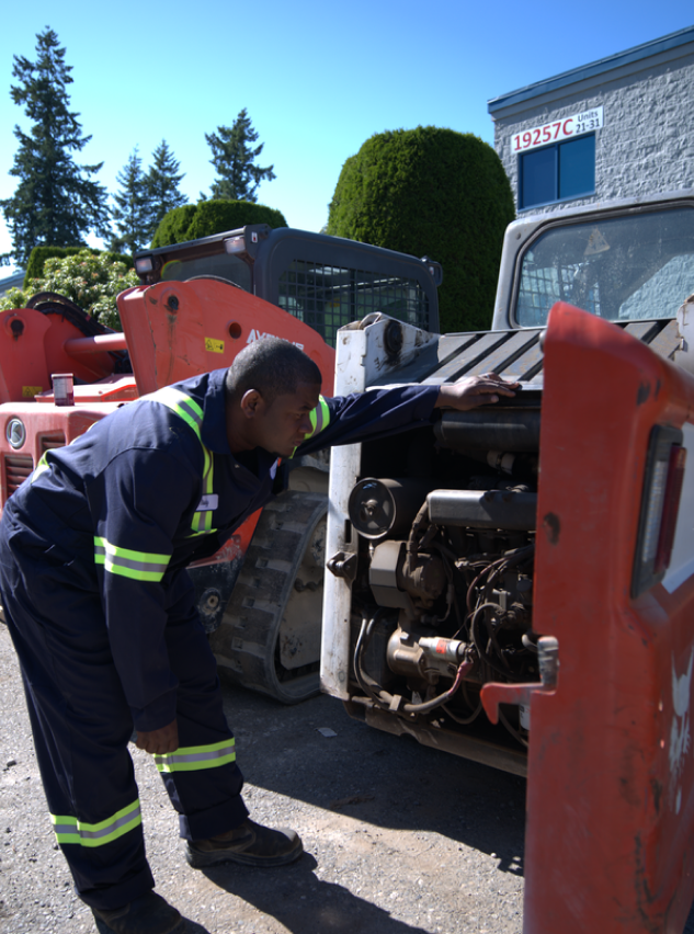 A skilled mechanic in a crisp blue uniform meticulously inspects robust bobcat equipment, showcasing a perfect blend of technical expertise and precision.