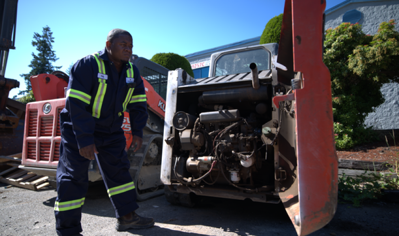 A mechanic carefully examines the intricate components of Bobcat machinery (Compact Construction Equipment Repair Services), conducting a thorough inspection to ensure optimal functionality and identifying any potential issues.